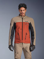 Alpinestars AMT-8 Stretch Drystar® XF Jas, Walnut Rust Black adventure touring motorjas, gedragen door een mannelijk model met bijpassende broek en handschoenen, voorzien van een driekleurig beige, roestbruin en zwart ontwerp met AMT-branding op de borst, actieve touring-pasvorm voor motorrijden