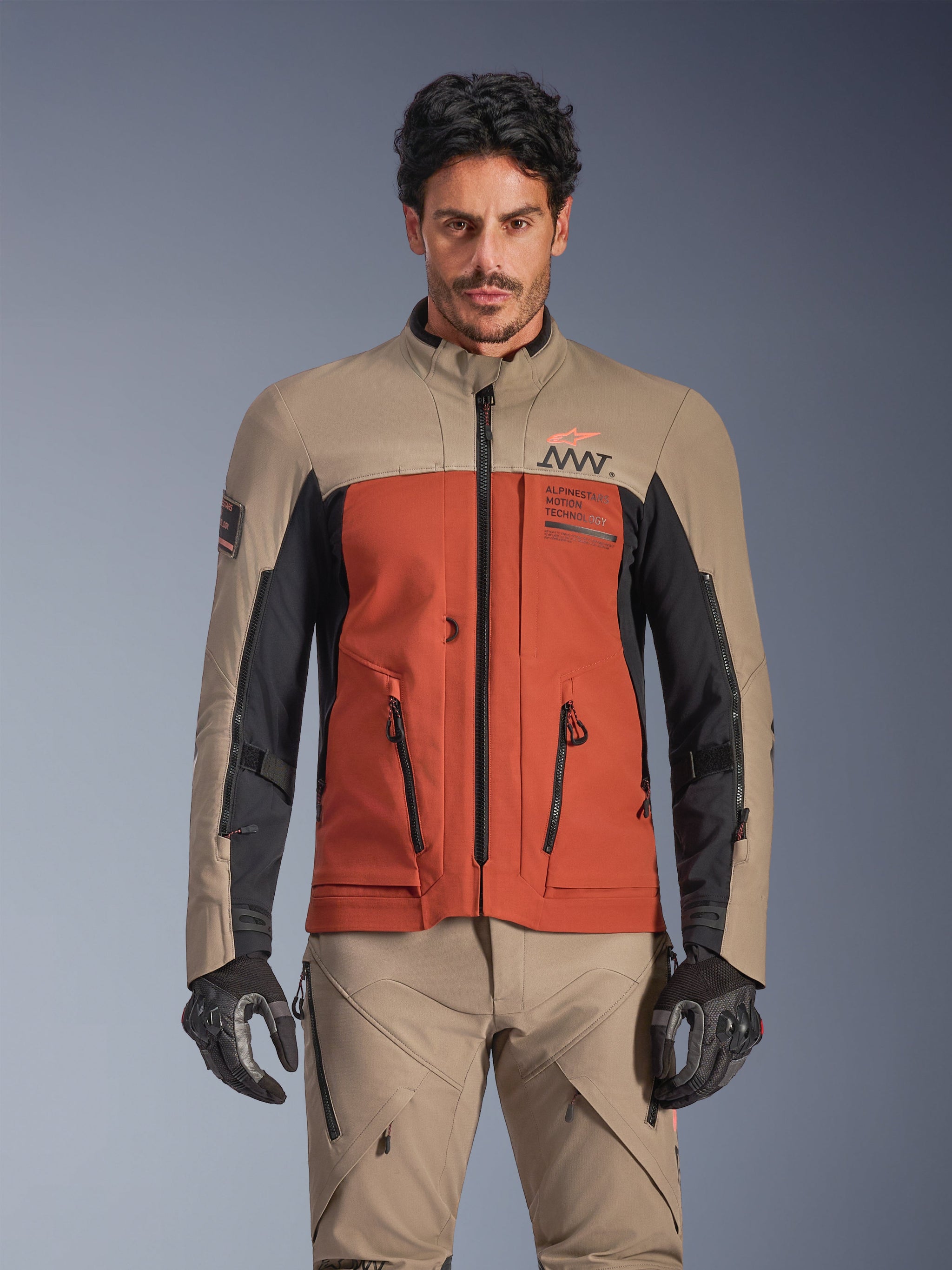 Alpinestars AMT-8 Stretch Drystar® XF Jacket, Walnut Rust Black adventure touring jacket, worn by male model with matching pants and gloves, featuring a tri-color tan, rust, and black design with AMT branding on the chest, active touring fit for motorcycle riding