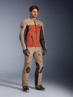 Alpinestars AMT-8 Stretch Drystar® XF Jas, Walnut Rust Black adventure-motorjas, gedragen met bijpassende technische broek en handschoenen, voorzien van een meerkleurig ontwerp met tan, roestoranje en zwarte panelen, ontworpen voor lange afstand motorreizen.