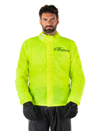 Alpinestars Hurricane Rain V2 Jacket, motorregenjas, neongeel, gedragen door een model met zwarte broek en handschoenen, hoge kraag met reflecterende tabs, stormflap aan de voorzijde met Alpinestars-logo, waterdichte kleding met hoge zichtbaarheid