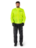 Alpinestars Hurricane Rain V2 jas en broek, neongeel en zwart, waterdicht motorregenpak gedragen met zwarte handschoenen en laarzen, voorzien van het Alpinestars-logo op de borst en het been
