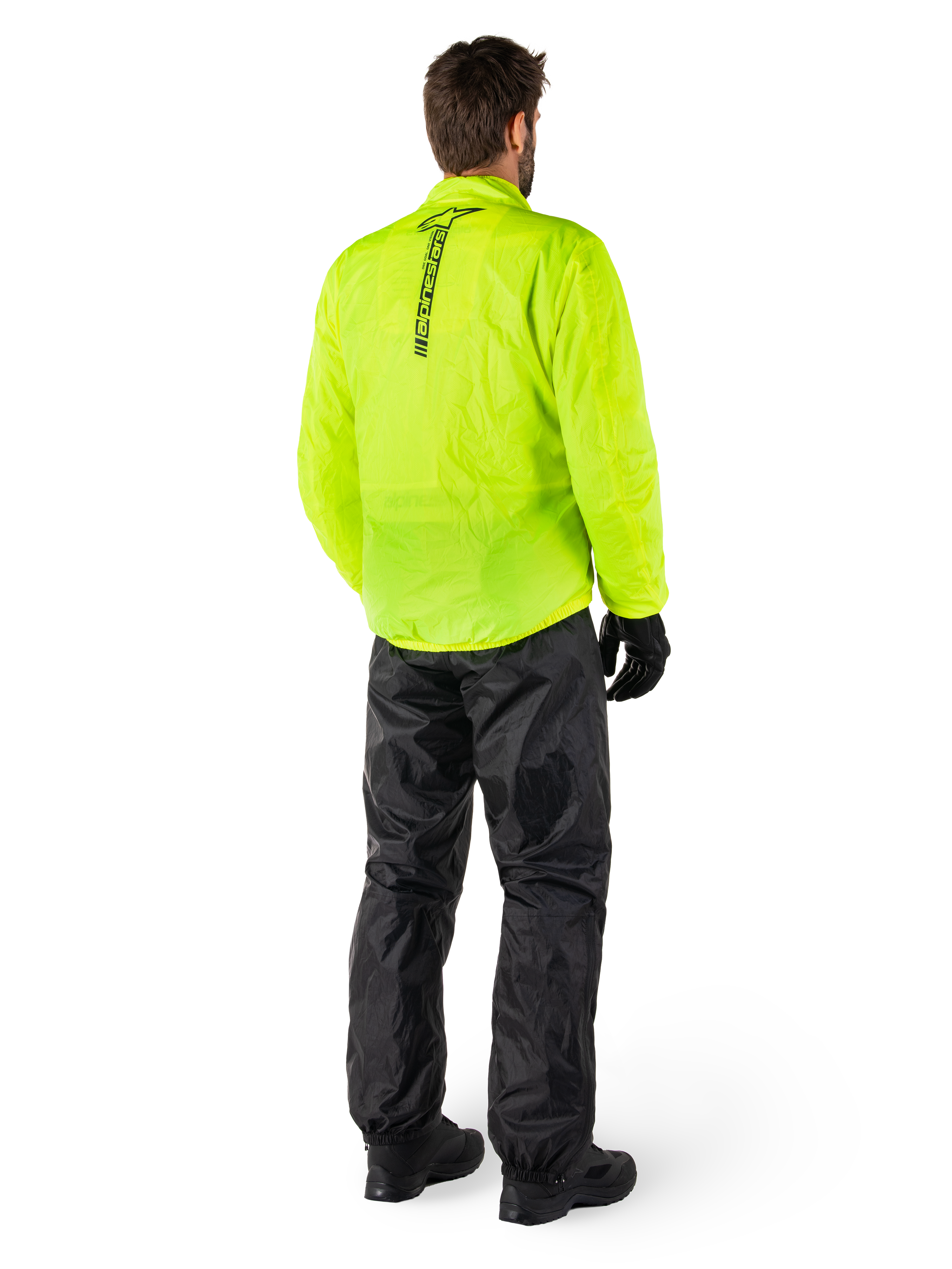 Alpinestars Hurricane Rain V2 Jacket in Yellow Fluo en Hurricane Rain V2 Pant in Black, persoon van achteren gezien, verticaal logo op de rug van de jas, waterdichte motorregenkleding met zwarte handschoenen en laarzen
