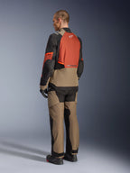 Alpinestars Andes V4 Drystar® Jas in Walnut Rust Black, model van achteren gezien met bijpassende textielbroek, zwarte handschoenen en laarzen, voorzien van een technisch multi-paneel ontwerp voor adventure touring en Alpinestars-branding.