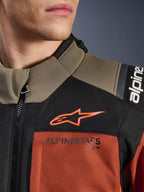Alpinestars Andes V4 Drystar® Jas in Walnut Rust Black, close-up van de bovenborst en schouder, met oranje A-star logo op zwart paneel en Alpinestars-branding op roestkleurig gedeelte, detail van adventure motoruitrusting