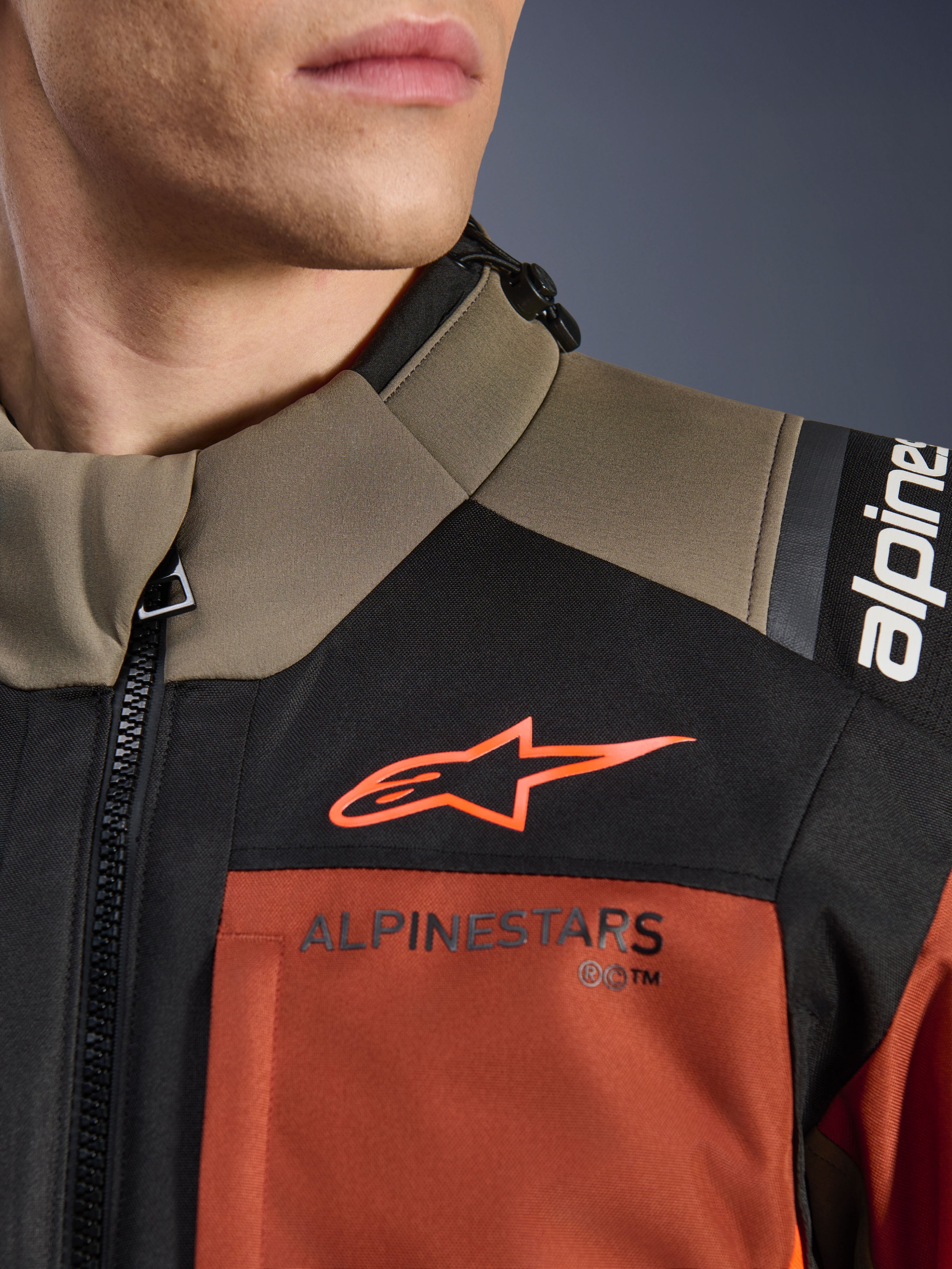 Alpinestars Andes V4 Drystar® Jas in Walnut Rust Black, close-up van de bovenborst en schouder, met oranje A-star logo op zwart paneel en Alpinestars-branding op roestkleurig gedeelte, detail van adventure motoruitrusting