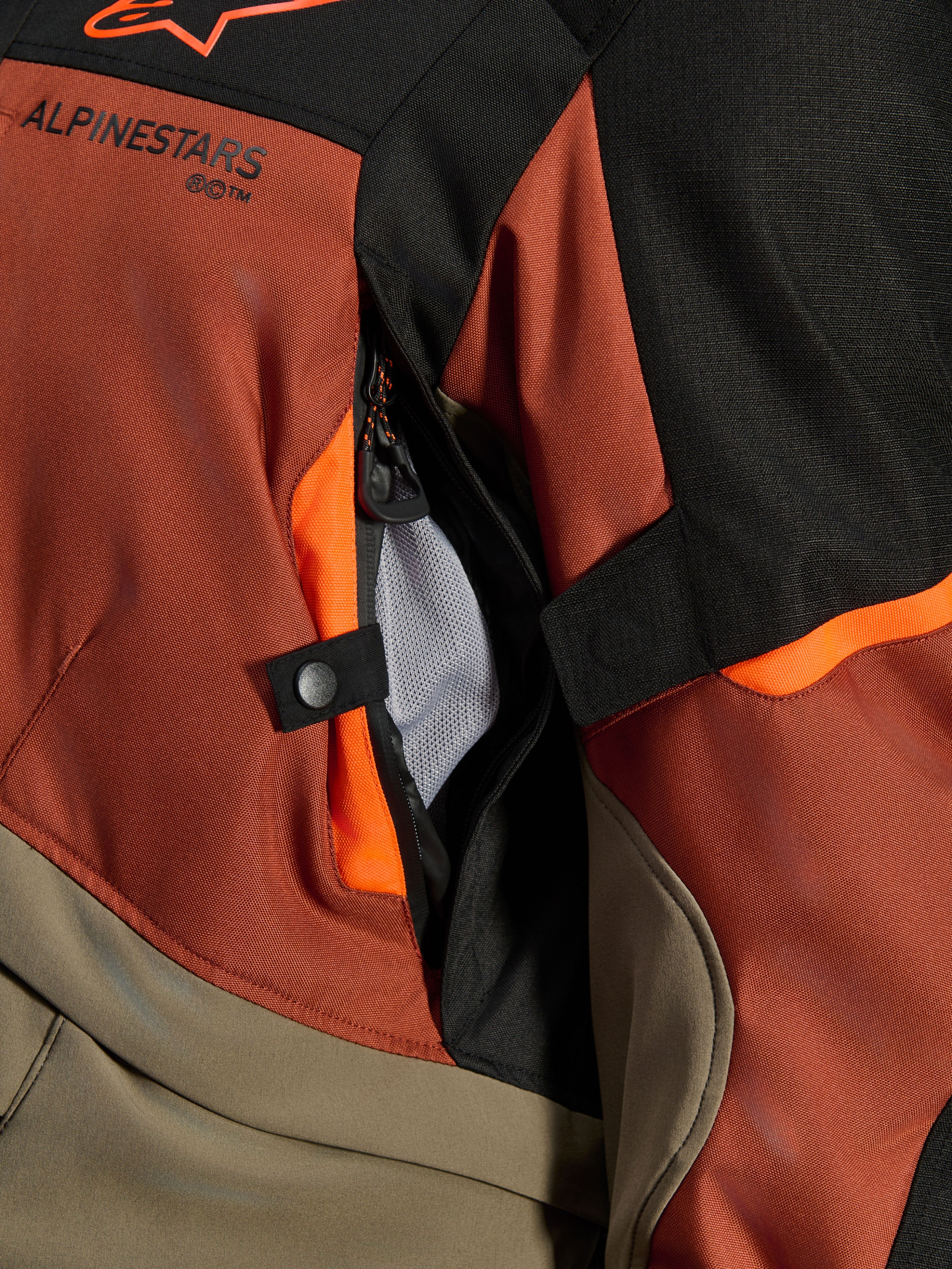 Alpinestars Andes V4 Drystar® Jas, Walnut Rust Black, close-up van directe ventilatieopening met mesh voering, duurzaam textielmateriaal met oranje accenten, drukknop en Alpinestars logo-detail