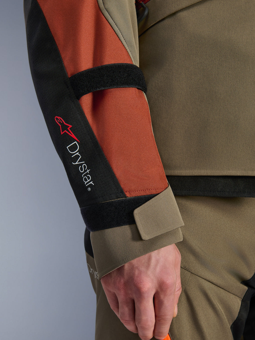 Alpinestars Andes V4 Drystar® Jas, motorjas, Walnut Rust Black, close-up van de mouw met Drystar®-branding en rood sterlogo, voorzien van verstelbare klittenbandsluitingen op de onderarm en pols, duurzaam adventure touring textielontwerp