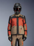 Alpinestars Andes V4 Drystar® jas, adventure motorjas, Walnut Rust Black, gedragen met een bijpassende helm en handschoenen, voorzien van een technisch multi-paneel ontwerp in beige, roestoranje en zwart met oranje branding en waterdichte ritsen.