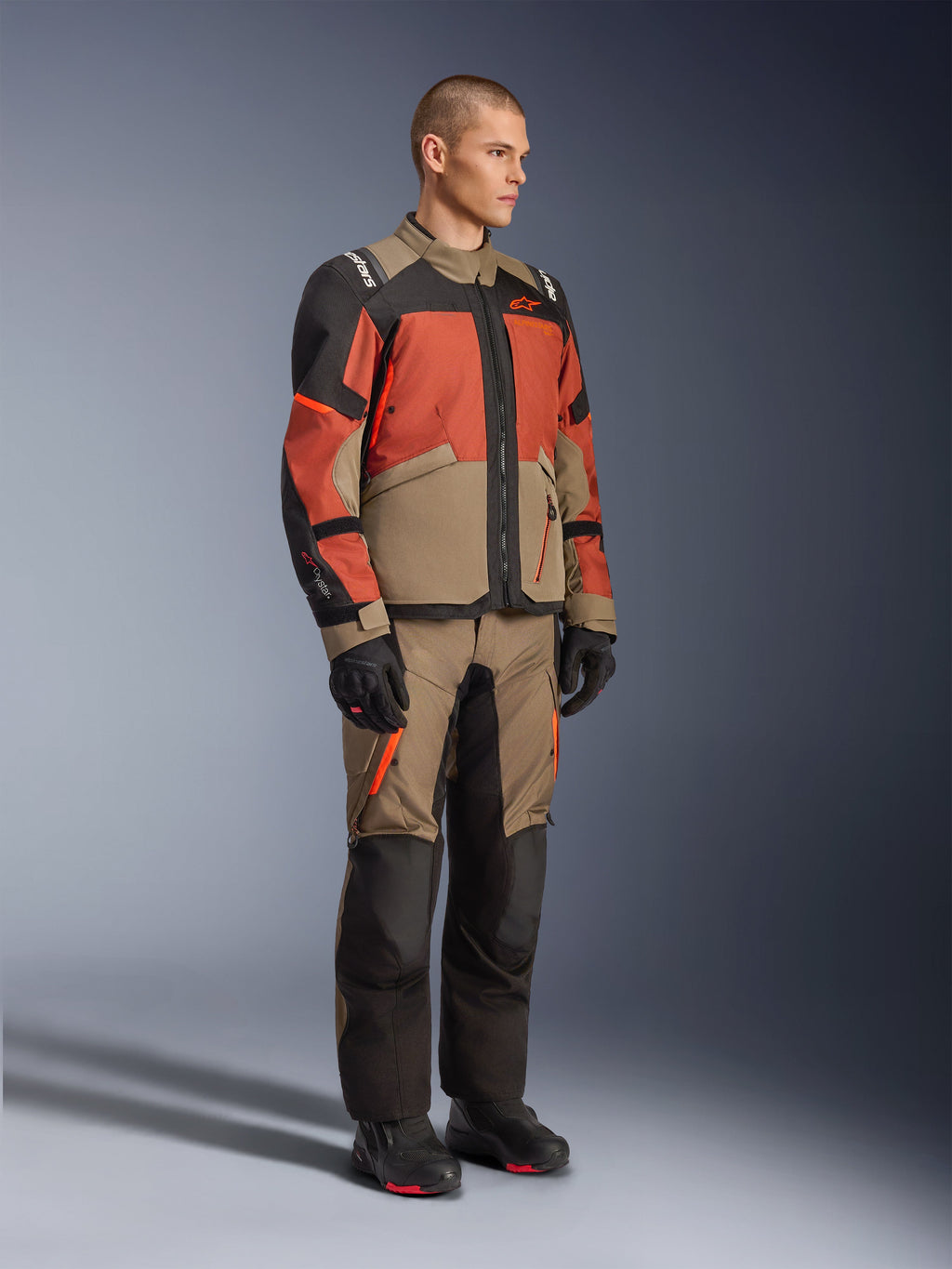 Alpinestars Andes V4 Drystar® Jas, adventure touring jas, Walnut Rust Black, gedragen met bijpassende broek en zwarte laarzen, met een kleurvlakken-ontwerp in beige, roestbruin en zwart, duurzame textielconstructie met zichtbare ritsen en Alpinestars-logo's.