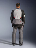 Alpinestars Andes V4 Drystar® Jas, adventure motorjas, donkergrijs, ijsgrijs, zwart en felrood, achteraanzicht van een rijder die een bijpassende broek draagt, voorzien van een groot ijsgrijs rugpaneel met rood logo, zwarte verstevigde schouderstukken en verstelbare tailleriemen voor touring in alle weersomstandigheden