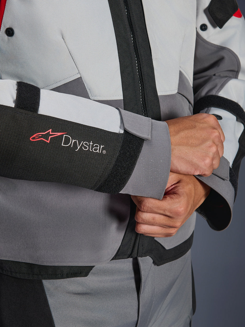 Close-up detail van de mouw van de Alpinestars Andes V4 Drystar® jas, grijs en zwart textiel, voorzien van een rood en wit Drystar-logo op de onderarm, verstelbare klittenbandsluiting bij de pols, hoogwaardige waterdichte motorkleding
