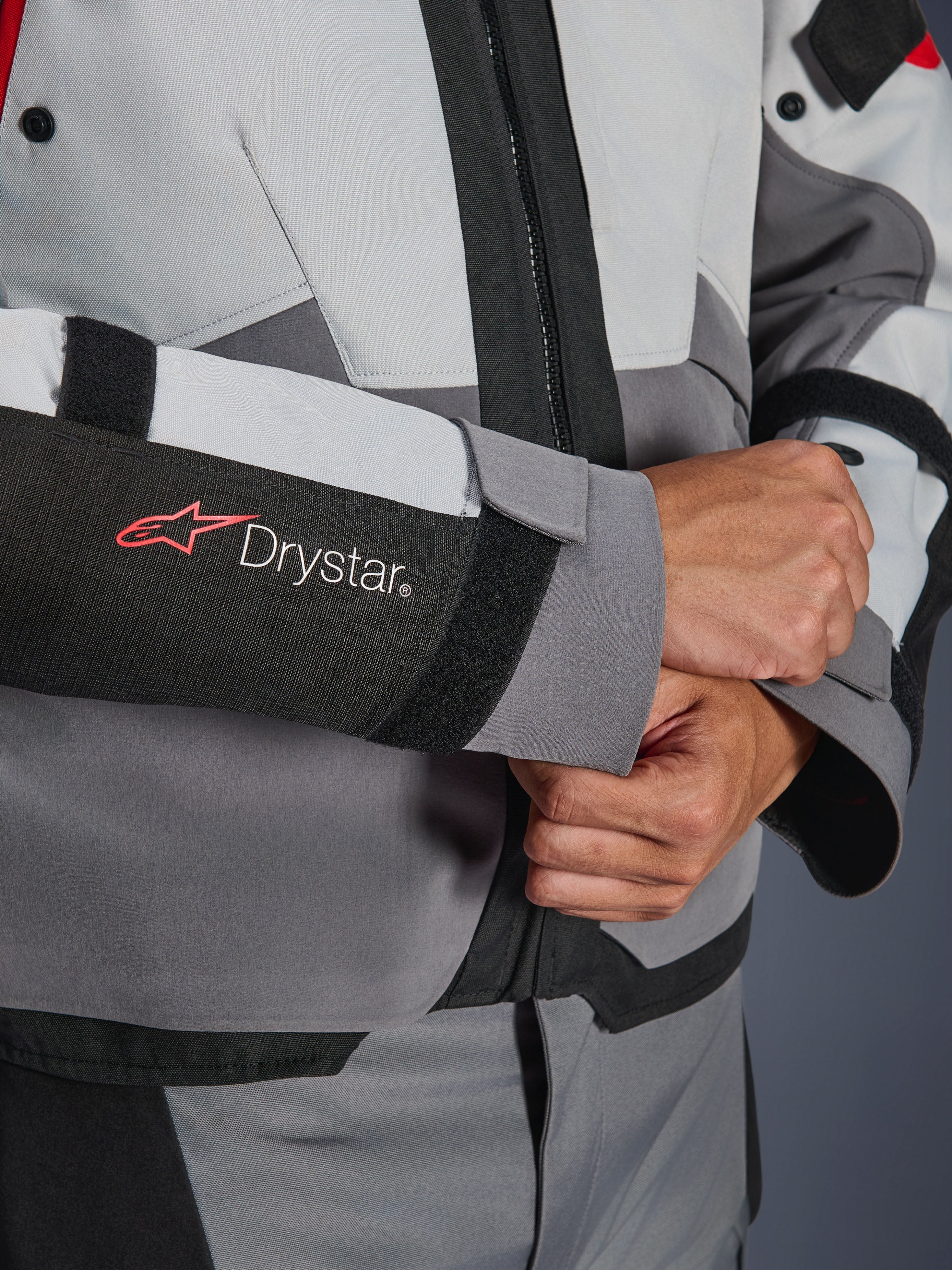 Close-up detail van de mouw van de Alpinestars Andes V4 Drystar® jas, grijs en zwart textiel, voorzien van een rood en wit Drystar-logo op de onderarm, verstelbare klittenbandsluiting bij de pols, hoogwaardige waterdichte motorkleding