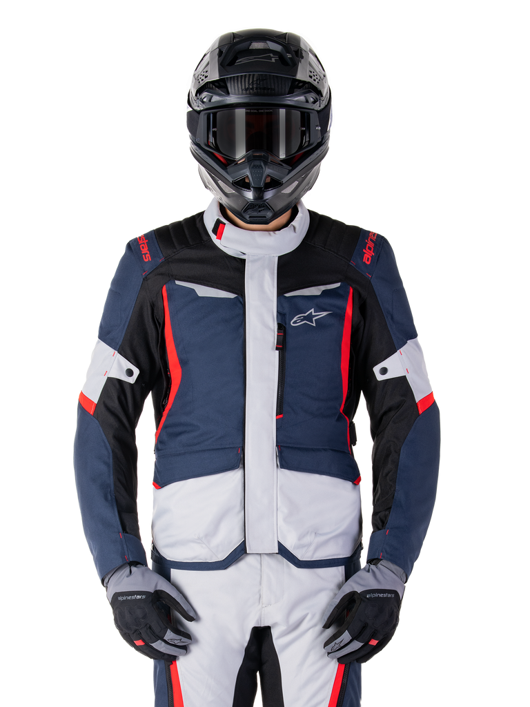 Alpinestars ST-1 Waterproof Jacket, adventure touring jas, donkerblauw, zwart en felrood, gedragen met een zwarte adventure helm en grijze handschoenen, voorzien van lichtgrijze panelen en rode accenten op de schouders en ritsen, strak ontwerp met Alpinestars-branding op de borst, duurzame waterdichte motorkleding