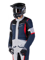 Alpinestars ST-1 Waterproof Jacket, adventure touring motorjas in donkerblauw, zwart en felrood, gedragen met een zwarte helm en grijze handschoenen, voorzien van een modern design met functionele zakken en Alpinestars-branding.