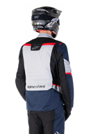 Alpinestars ST-1 Waterproof Jacket, donkerblauw, zwart en felrood, achteraanzicht van een rijder met een zwarte adventure-helm, voorzien van lichtgrijze panelen en Alpinestars-branding, adventure touring motorkleding