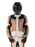Alpinestars ST-1 Waterproof jas, Dark Khaki Sand Black Red Fluo, gedragen door een motorrijder met een zwarte helm en handschoenen, adventure touring motorkleding met beige en bruine panelen en felle fluo rode accenten, vooraanzicht op een witte achtergrond.