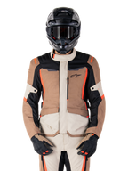 Alpinestars ST-1 Waterproof jas, Dark Khaki Sand Black Red Fluo, gedragen door een motorrijder met een zwarte helm en handschoenen, adventure touring motorkleding met beige en bruine panelen en felle fluo rode accenten, vooraanzicht op een witte achtergrond.