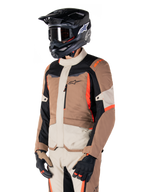 Alpinestars ST-1 Waterproof jas, adventure touring-jas, Dark Khaki Sand Black en Red Fluo, gedragen door een rijder met een zwarte motorcrosshelm en bril, voorzien van een multi-panel ontwerp met cargozakken en Alpinestars-branding op de borst