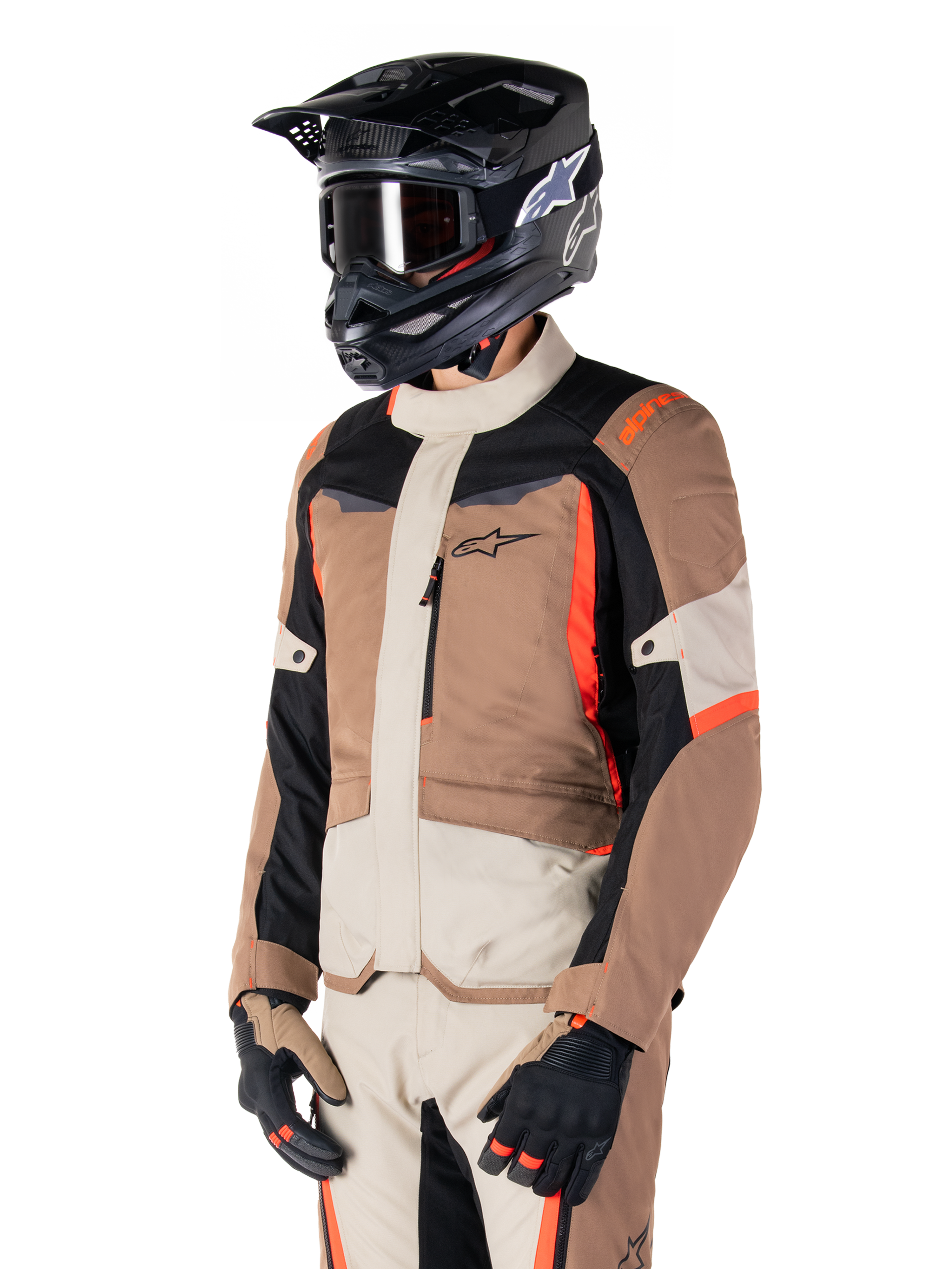 Alpinestars ST-1 Waterproof jas, adventure touring-jas, Dark Khaki Sand Black en Red Fluo, gedragen door een rijder met een zwarte motorcrosshelm en bril, voorzien van een multi-panel ontwerp met cargozakken en Alpinestars-branding op de borst