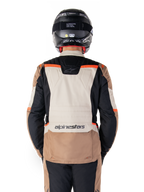 Alpinestars ST-1 Waterproof Jas, Dark Khaki Sand Black Red Fluo, achteraanzicht, adventure touring motorjas met een groot zandkleurig rugpaneel, zwarte mouwen en rode fluo accenten, gedragen door een motorrijder met een zwarte helm