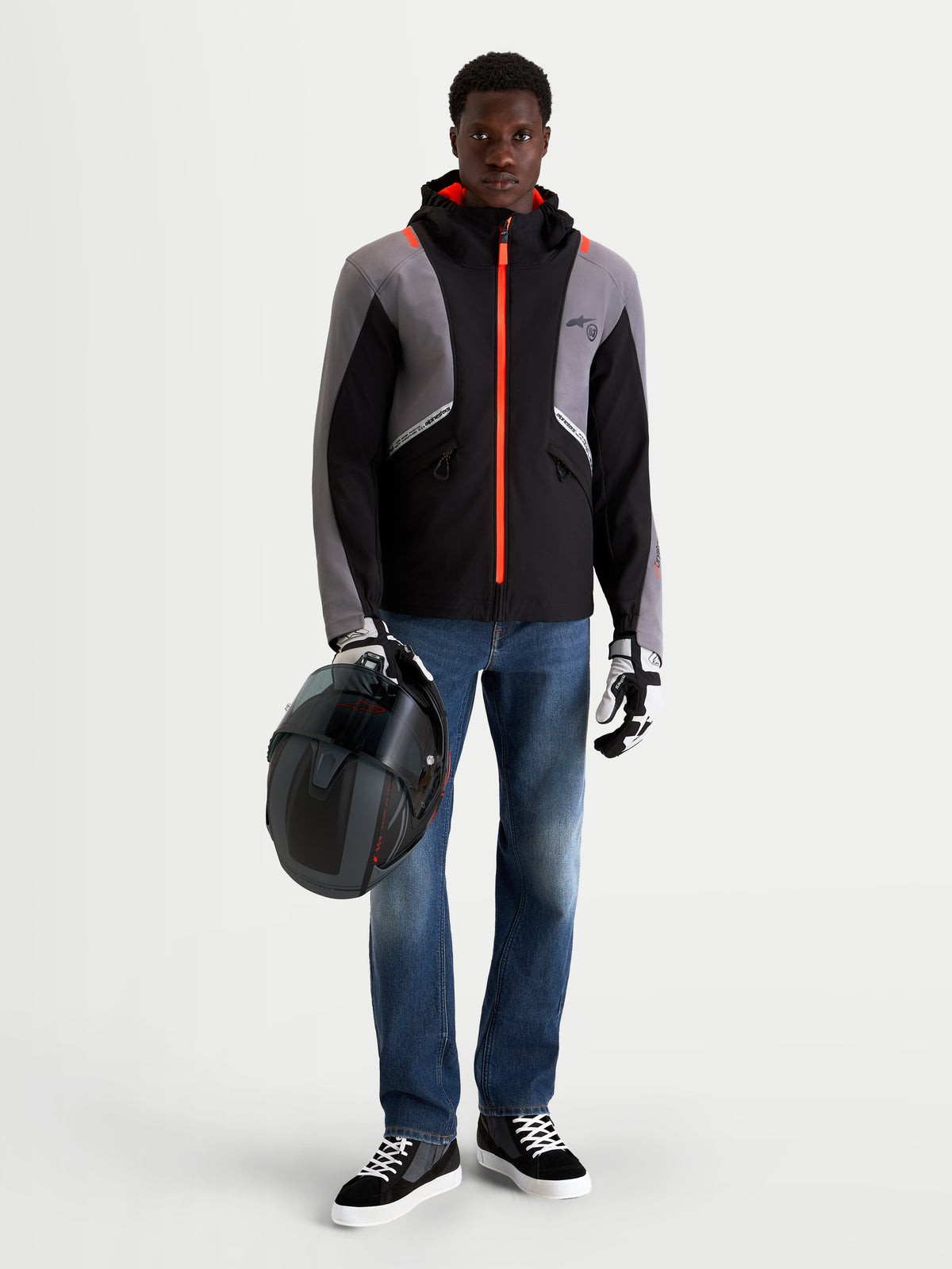Alpinestars C 5 Drystar jas, heren urban contemporary motorjas in zwart en donkergrijs, vooraanzicht op model met jeans, handschoenen en helm, terwijl hij een helm vasthoudt