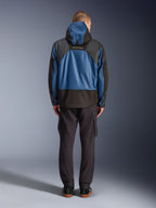Alpinestars Mospher Waterproof jas in zwart en Dark Petrol, achteraanzicht op model, gecombineerd met een zwarte cargobroek, voorzien van tactische ripstop-constructie en MO.ST.EQ.-branding op de rug