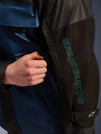 Alpinestars Mospher Waterproof Jas in Black Dark Petrol, close-up detail van de mouw met petrolblauwe Alpinestars-branding, een hand die de ventilatierits aanpast, voorzien van duurzame ripstop-stof en een verstelbare mouwband