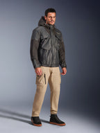 Mannelijk model draagt de Alpinestars Mospher Waterproof Jacket in het zwart, een op utility geïnspireerde waterdichte parka met een multi-pocket design en capuchon, gecombineerd met een beige cargobroek en zwarte high-top sneakers, stedelijke motoruitrusting voor woon-werkverkeer.