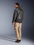 Alpinestars Mospher Waterproof Jacket in het zwart, man in achteraanzicht en zijprofiel, gecombineerd met een beige cargobroek en zwarte sneakers, parka-ontwerp met capuchon, ripstop-stof, Alpinestars-logo op de mouw, moderne urban motorstijl.