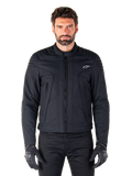 Alpinestars Clayton WR Jacket, zwarte motorjas, gedragen door een model, voorzien van gewatteerde schouderdetails en technische graphics, centrale Vislon-rits, verticale zakken met rits, klein wit logo op de borst, stedelijke motorkleding voor weggebruik