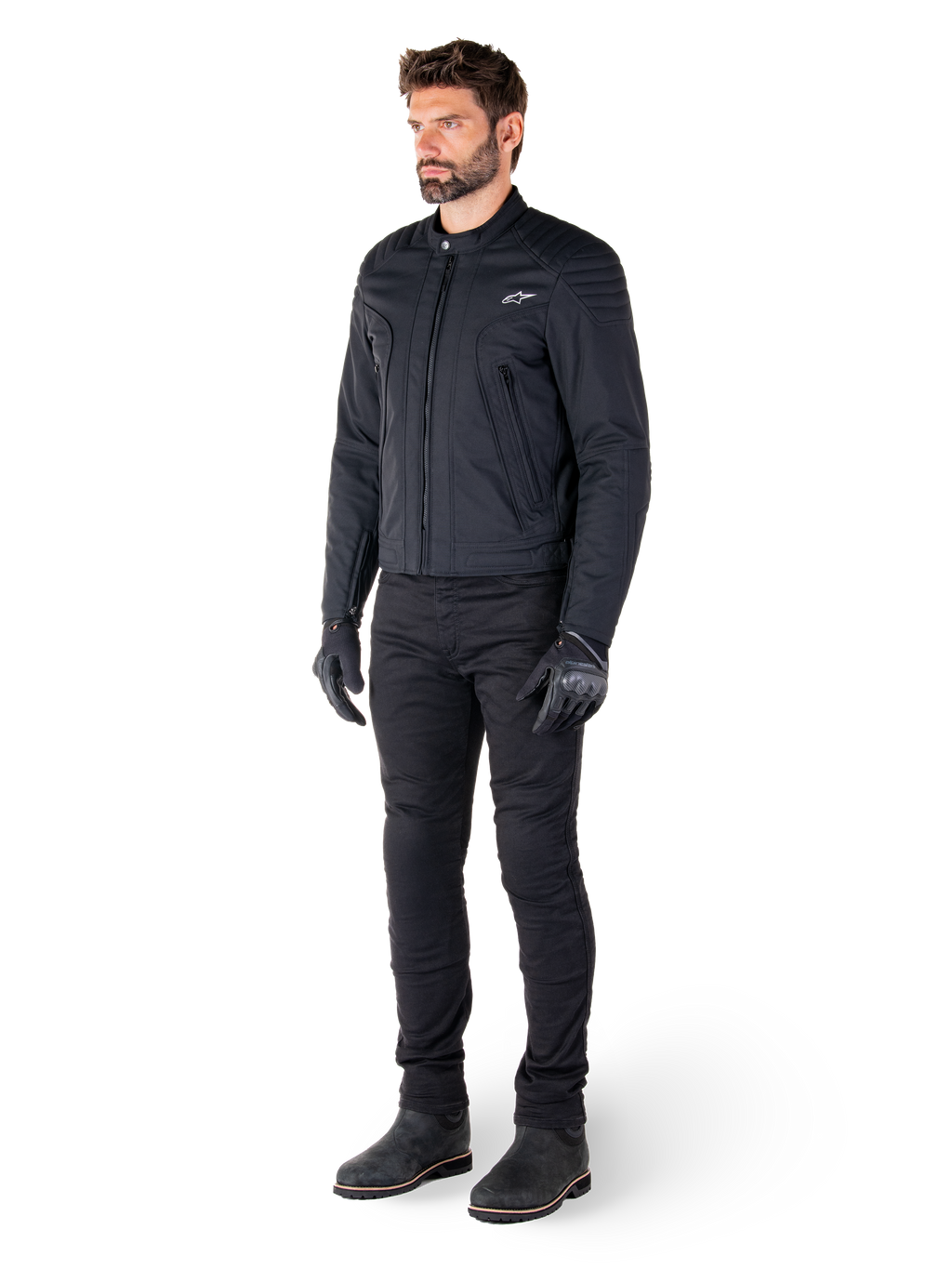 Mannelijke motorrijder die de Alpinestars Clayton WR jas draagt, zwarte urban motorjas, slim-fit ontwerp met gewatteerde schouderaccenten en matte afwerking, gecombineerd met een zwarte technische motorbroek en handschoenen.
