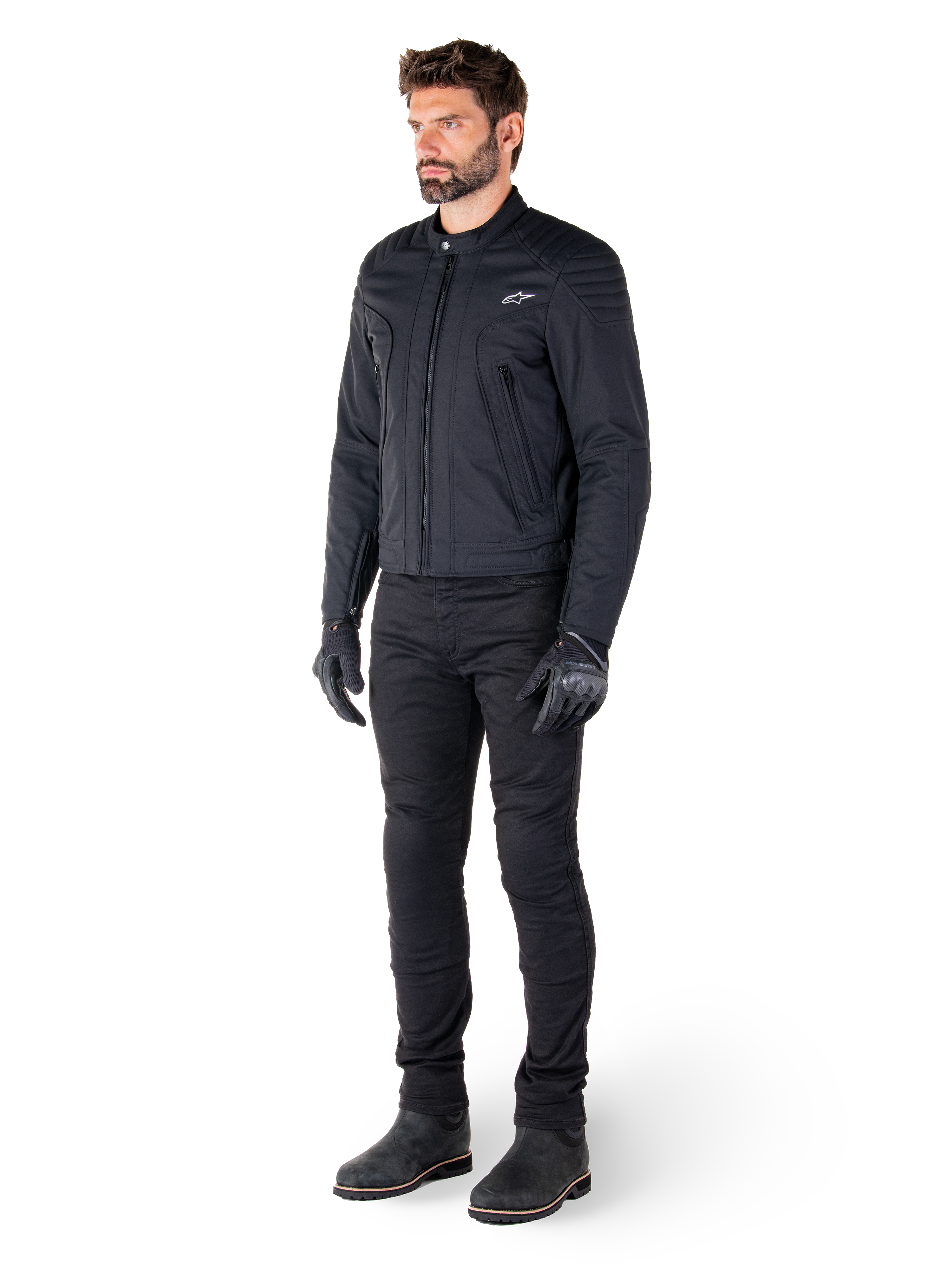 Mannelijke motorrijder die de Alpinestars Clayton WR jas draagt, zwarte urban motorjas, slim-fit ontwerp met gewatteerde schouderaccenten en matte afwerking, gecombineerd met een zwarte technische motorbroek en handschoenen.