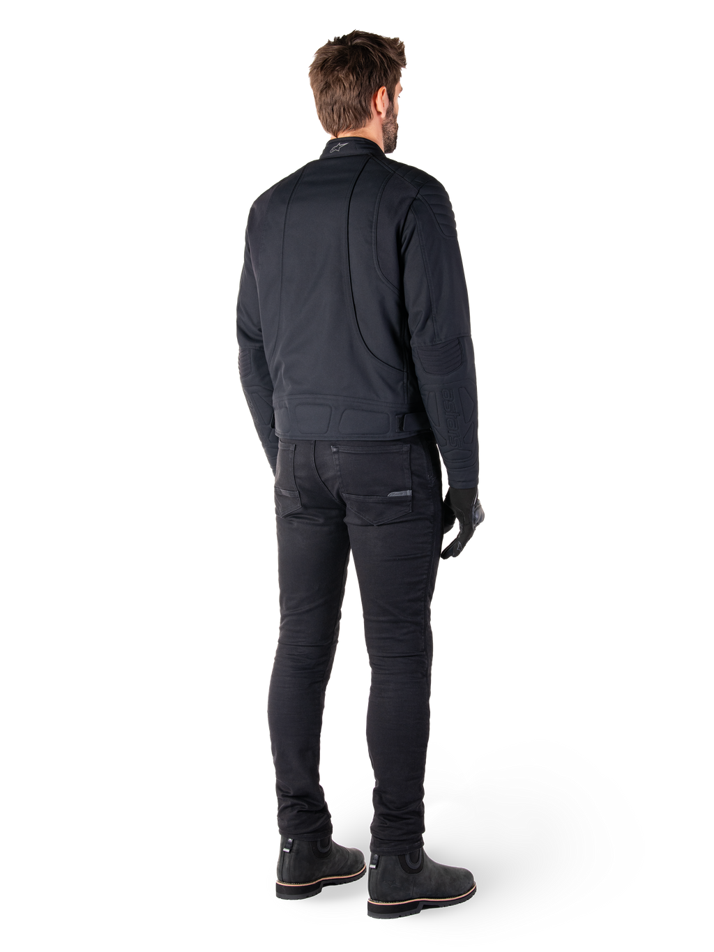 Achteraanzicht van een motorrijder die de Alpinestars Clayton WR Jas in het zwart draagt, voorzien van gewatteerde elleboog- en schouderpanelen, ergonomische gebogen stiknaden en reflecterende kraagdetails, gecombineerd met een zwarte motorbroek en laarzen voor een urban motorlook.