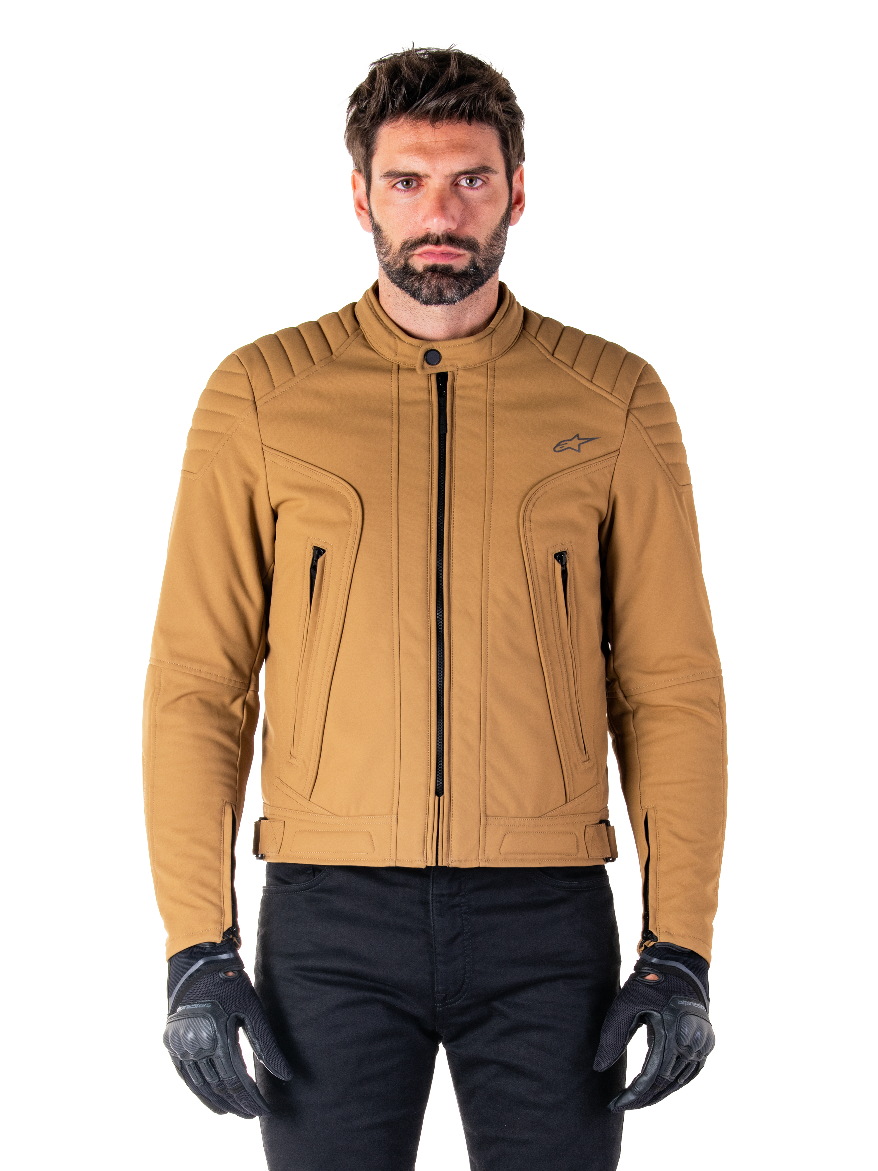 Alpinestars Clayton WR jas, urban motorjas, Utility Brown Light Gold, waterbestendig textiel met gewatteerde schouders, hoge kraag, zwarte ritsdetails en logo op de borst, gedragen met zwarte beschermende handschoenen en broek