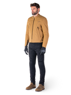 Mannelijke motorrijder draagt de Alpinestars Clayton WR Jas in Utility Brown Light Gold, een urban contemporary motorjas met gewatteerde schouderdetails, gecombineerd met een zwarte broek, zwarte handschoenen en bruine laarzen