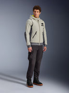 Alpinestars Moblast Waterproof Jacket, Iron Gray and Dark Sage, urban motorcycle riding jacket with a hoodie design, worn by a model with dark riding pants and black boots, minimalist cyber-tech aesthetic with a yellow interior hood and waterproof zippers