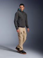 Mannelijk model draagt Alpinestars Moblast Waterproof Jas in het zwart, stedelijke motorhoodie met blauwgroen gevoerde capuchon, gecombineerd met een kaki cargobroek en zwarte sneakers, modern minimalistisch ontwerp met technische stretchstof voor woon-werkverkeer in alle weersomstandigheden