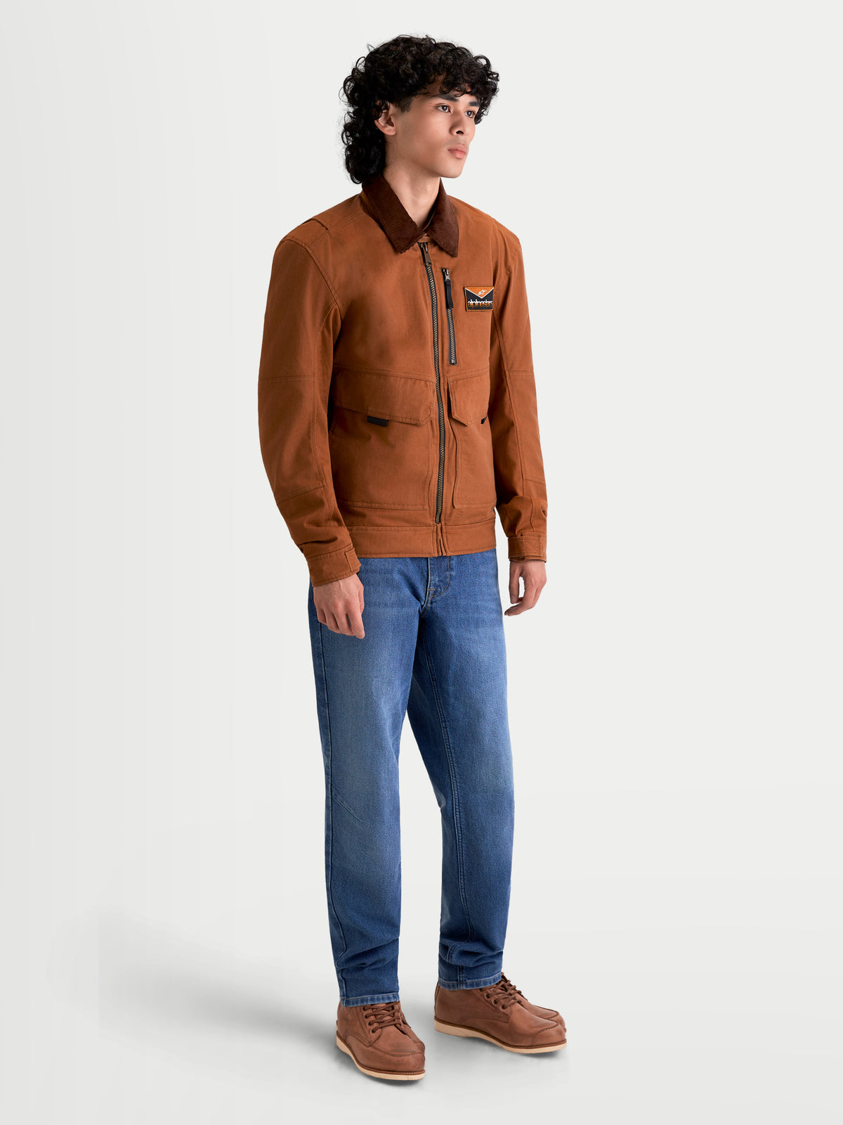 Alpinestars Mustang WP jas, urban motorjas voor heren in donkerroestbruin en donkerbruin, zijprofiel op een model in werkkleding-stijl en blauwe jeans