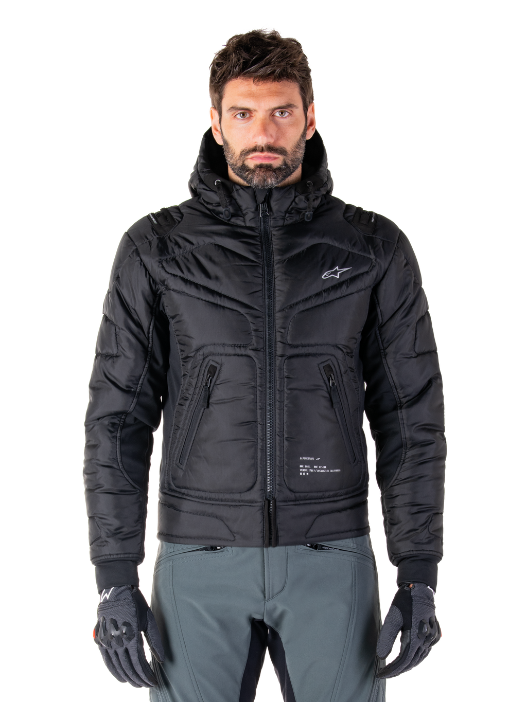 Alpinestars Mohobbs Waterproof Jacket, zwarte gewatteerde bomber motorjas, gewatteerde poly-stof met ritssluiting en ritszakken, klein wit logo op de borst, gedragen door een model met grijze broek en handschoenen, urban streetwear-ontwerp voor rijden in de stad
