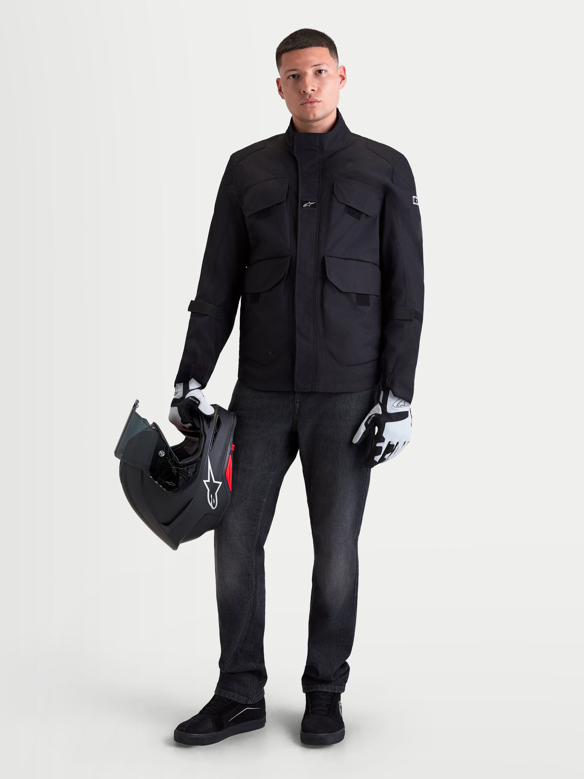 Alpinestars Altan Drystar jas, heren urban motorjas in zwart, vooraanzicht op model met helm en motorhandschoenen, waterdichte textiel jas met cargozakken