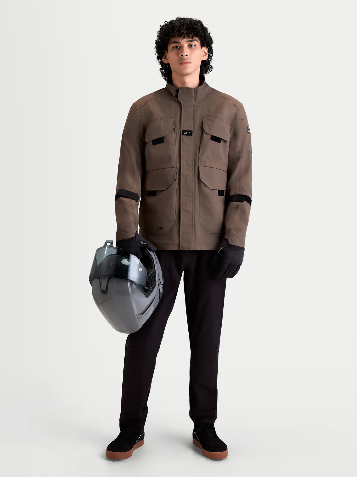 Alpinestars Altan Drystar Jas, urban herenmotorjas in walnootbruin, vooraanzicht op model met zwarte broek, handschoenen en helm, waterdichte textielconstructie met cargozakken