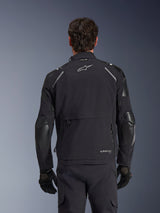 Alpinestars Andes Pro Drystar® XF jas, zwart en donkergrijs, achteraanzicht gedragen door een mannelijk model, met een groot opbergcompartiment aan de achterzijde, reflecterende schouderaccenten en merklogo's, gecombineerd met zwarte handschoenen en broek voor adventure touring
