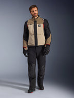 Mannelijk model draagt Alpinestars Andes Pro Drystar® XF Jacket in Walnut Aluminum, zandkleurige en zwarte adventure touring jas met rode accenten, zwarte motorbroek, handschoenen en laarzen, studio-opname van het volledige lichaam, beschermende motorkleding