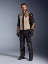 A male model wearing the Alpinestars Andes Pro Drystar® XF Jacket in Walnut Aluminum, paired with black motorcycle pants, gloves, and boots, featuring a tan and black multi-panel design with red accents for adventure touring.