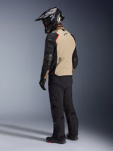 Motorcycle rider from behind wearing the Alpinestars Andes Pro Drystar® XF Jacket in Walnut Aluminum, featuring a tan back panel with black sleeves and red accents, black adventure helmet, black riding pants, and black boots, professional adventure touring gear.
