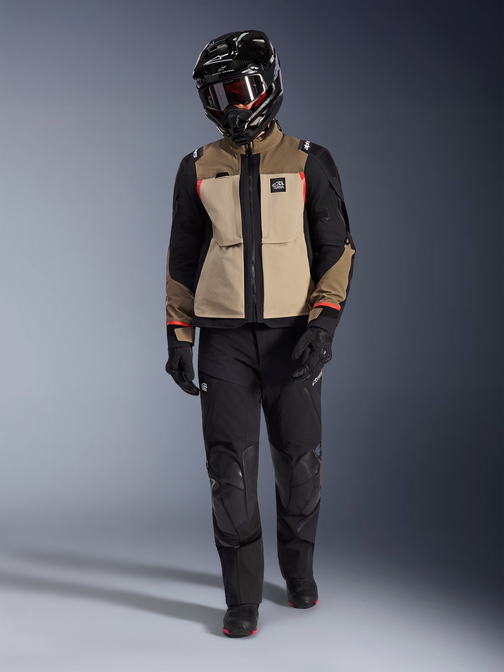 Alpinestars Andes Pro Drystar® XF Jacket in Walnut Aluminum, worn with black adventure pants, black gloves, and a black full-face helmet with goggles, featuring red highlights and All Terra branding, professional adventure touring setup