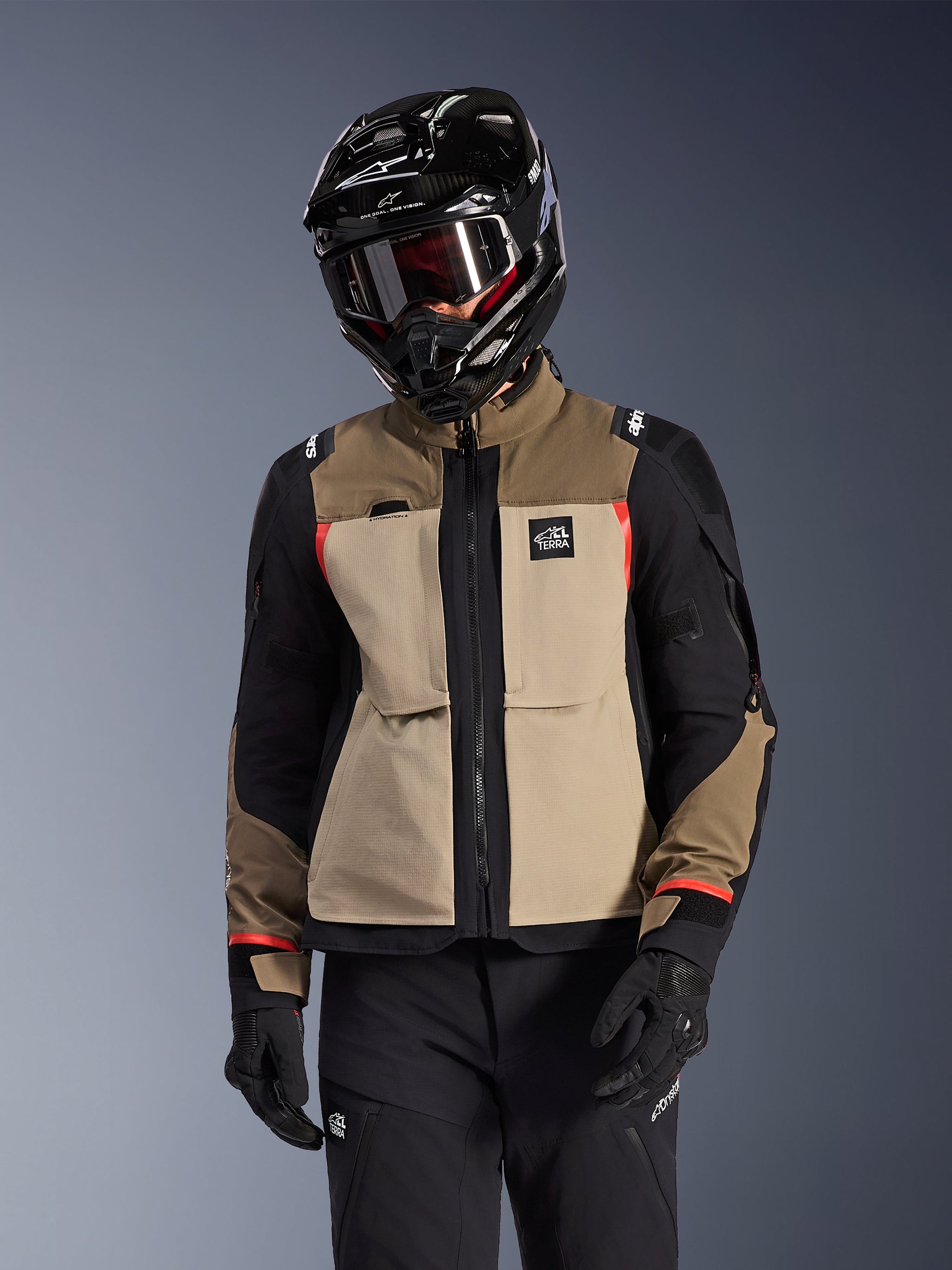 Alpinestars Andes Pro Drystar® XF Jacket, Adventure Touring Motorcycle Jacket, Walnut Aluminum beige and brown with black panels and red accents, worn with a black Alpinestars helmet and goggles, technical outdoor motorcycle gear