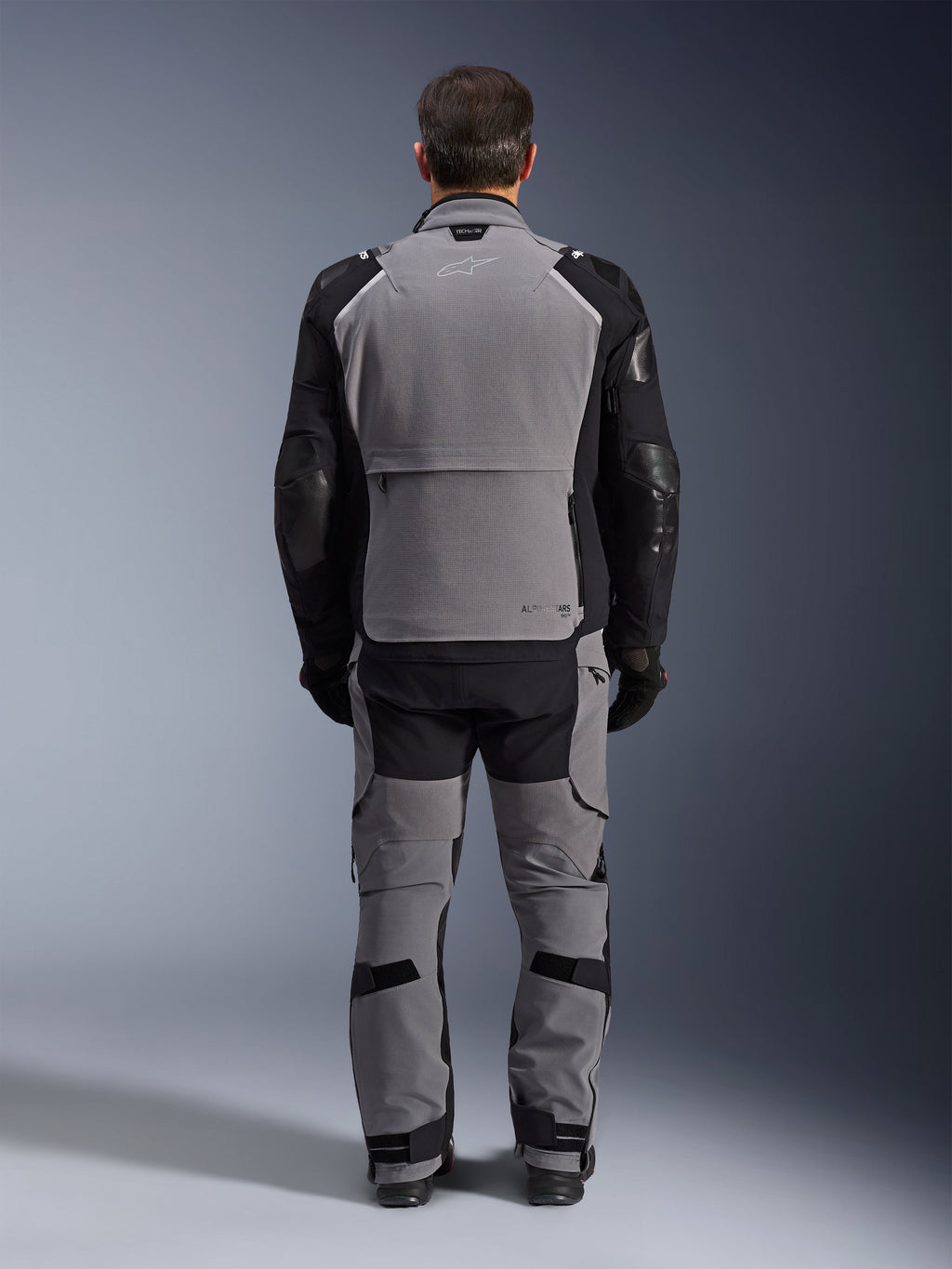 Alpinestars Andes Pro Drystar® XF Jacket, donkergrijs zwart, achteraanzicht van een motorrijder die een bijpassende broek draagt, adventure touring motorjas met een groot grijs rugpaneel, zwarte gearticuleerde mouwen met bescherming en een opbergvak aan de achterzijde