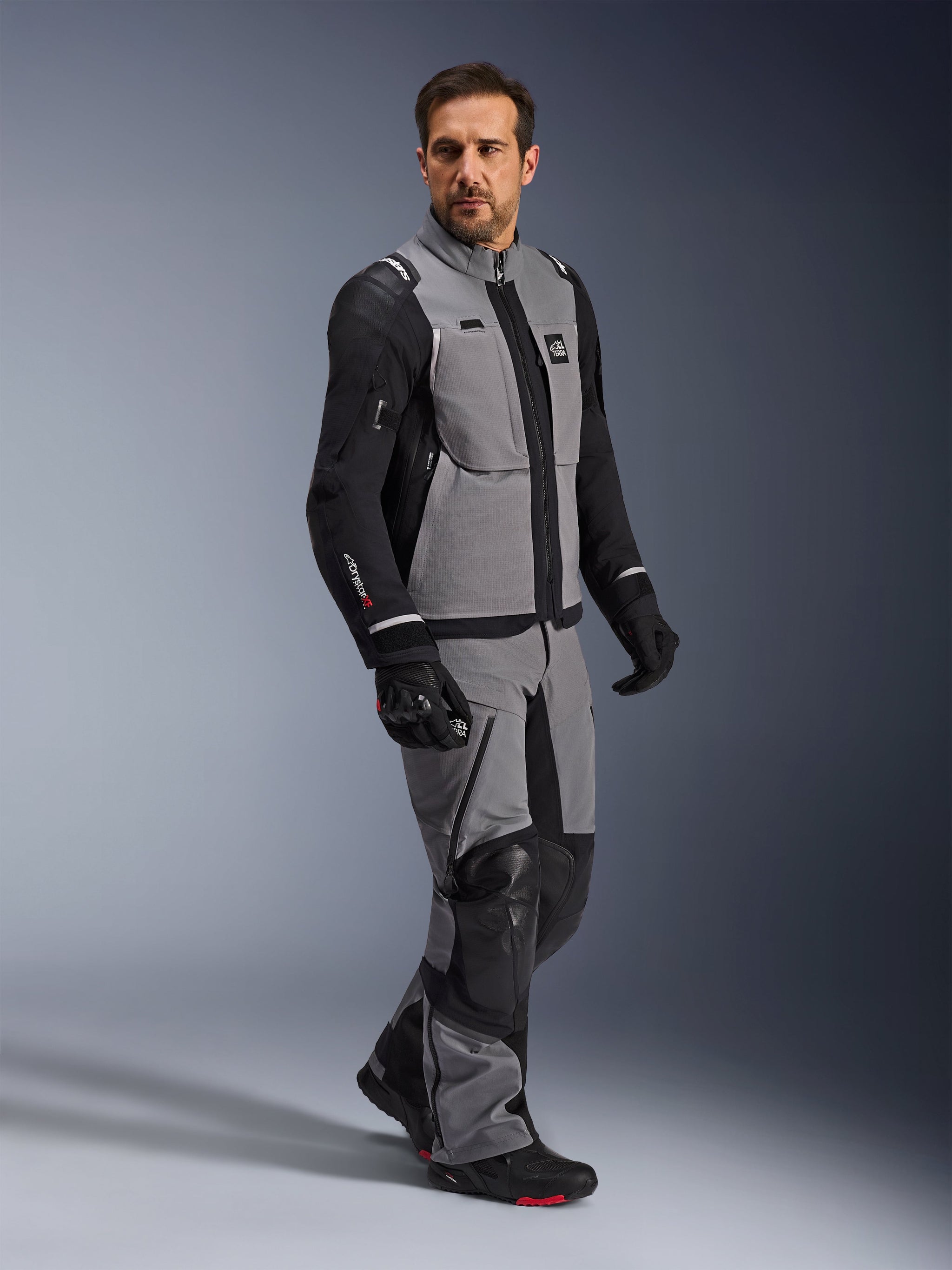 Alpinestars Andes Pro Drystar® XF Jacket, Adventure Motorcycle Jacket, Dark Gray and Black, worn by a model with matching textile pants and black gloves, featuring a multi-pocket design, technical 3-layer laminated shell, and articulated fit for long-distance adventure riding.