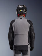 Alpinestars Andes Pro Drystar® XF Jas, donkergrijs en zwart, achteraanzicht met grote opbergzak op de rug en Tech-Air branding, gedragen door een motorrijder met een zwarte helm en bijpassende motorbroek, professionele adventure touring uitrusting